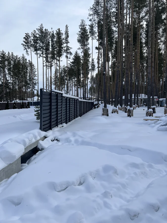 Поворот линии ограждения среди сосен зимой.
